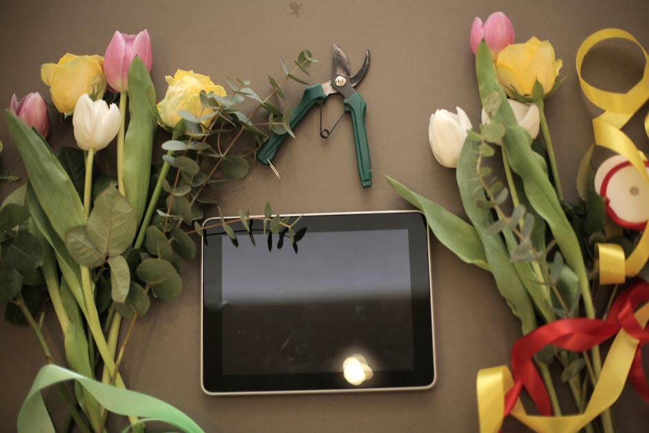 A flat lay composition showcases fresh tulips in pastel pink, creamy yellow, and white, arranged with green foliage on a neutral background. The flowers, with their petals fully open, display vibrant