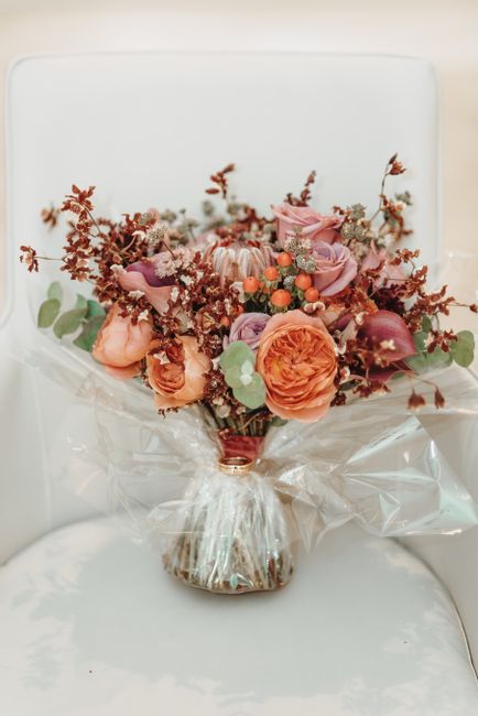 A fresh floral bouquet arranged in a small glass vase, featuring a harmonious mix of peach and pink roses, lavender-hued lisianthus, and clusters of orange berries, complemented by burgundy and dusty