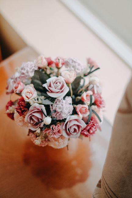 A close-up of a floral bouquet featuring soft pink roses, small white and pink spray roses, clusters of delicate white lilacs, and sprigs of muted green eucalyptus, arranged in a rounded, lush style.