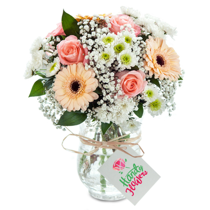Vividly capturing the spirit of Lee's leafy streets and community charm, this elegantly arranged bouquet presents a soft medley of blossoms in a classic clear vase. Dominating the centre are several peachy-pink roses-each one a study in floral perfection, with velvety petals softly curling outward and creating a romantic, timeless impression. Flanking them, two prominent gerbera daisies announce themselves with bright peach petals and rich brown centers, expressing the joy and friendship often felt along Lee's bustling pavements. Intermixed are airy, white clouds of baby's breath that breathe ethereal lightness into the arrangement, alongside small, crisp chrysanthemums, their subtle green centers a quiet nod to the natural beauty at Manor Park. Fresh eucalyptus and deep green leaves emerge at intervals, complementing the pastel tones while underpinning the bouquet with refreshing, earthy notes. Nestled securely in a slightly textured glass vase, the flowers' stems are visible through clear water-proof of their freshness and longevity. A rustic twine bind, deftly tied, loops around the vase's neck, suspending a neat white tag ready for any message or warm wish. The overall effect is one of gentle grace and joyful sincerity, making this bouquet a fitting gift for celebrating new beginnings, sending gratitude, or bringing a touch of local Lee artistry into any home.